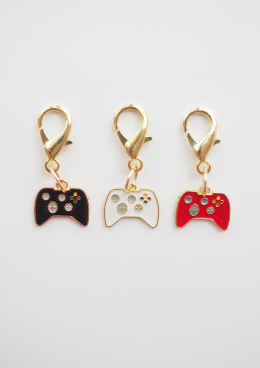 image of 3 stitch markers in the shape of game controllers. one black, one white, one red