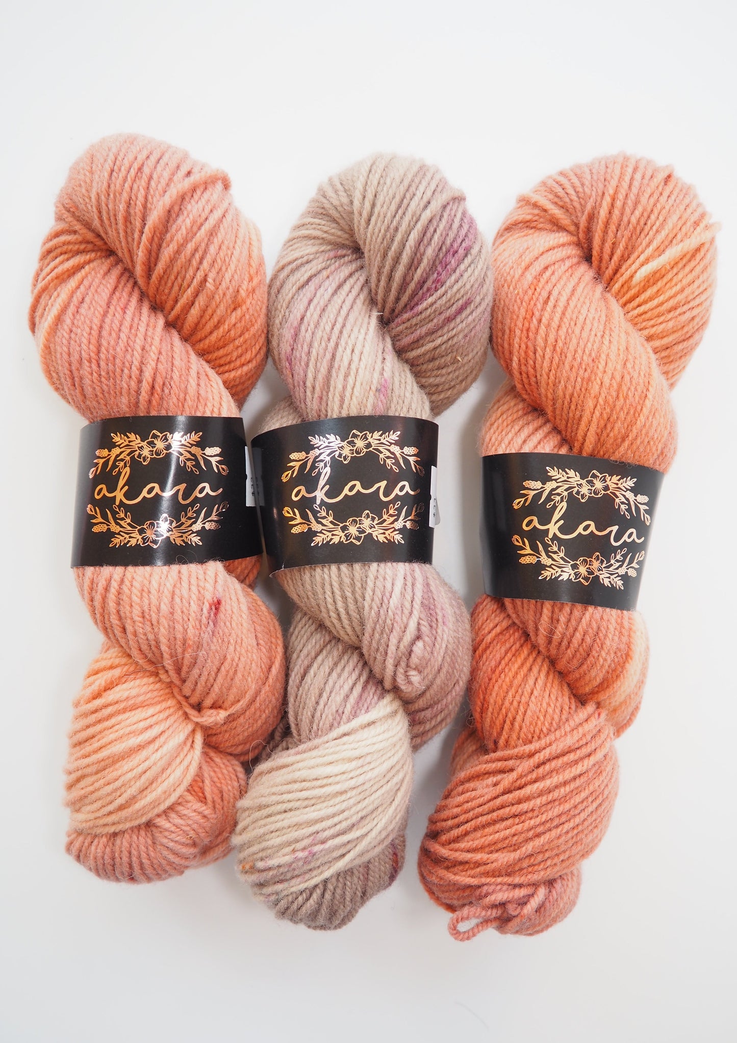 Image of three skeins of Akara Dorset Aran yarn, featuring one in Frozen Berries color and two in Rose Gold, displaying their vibrant colors and rustic texture