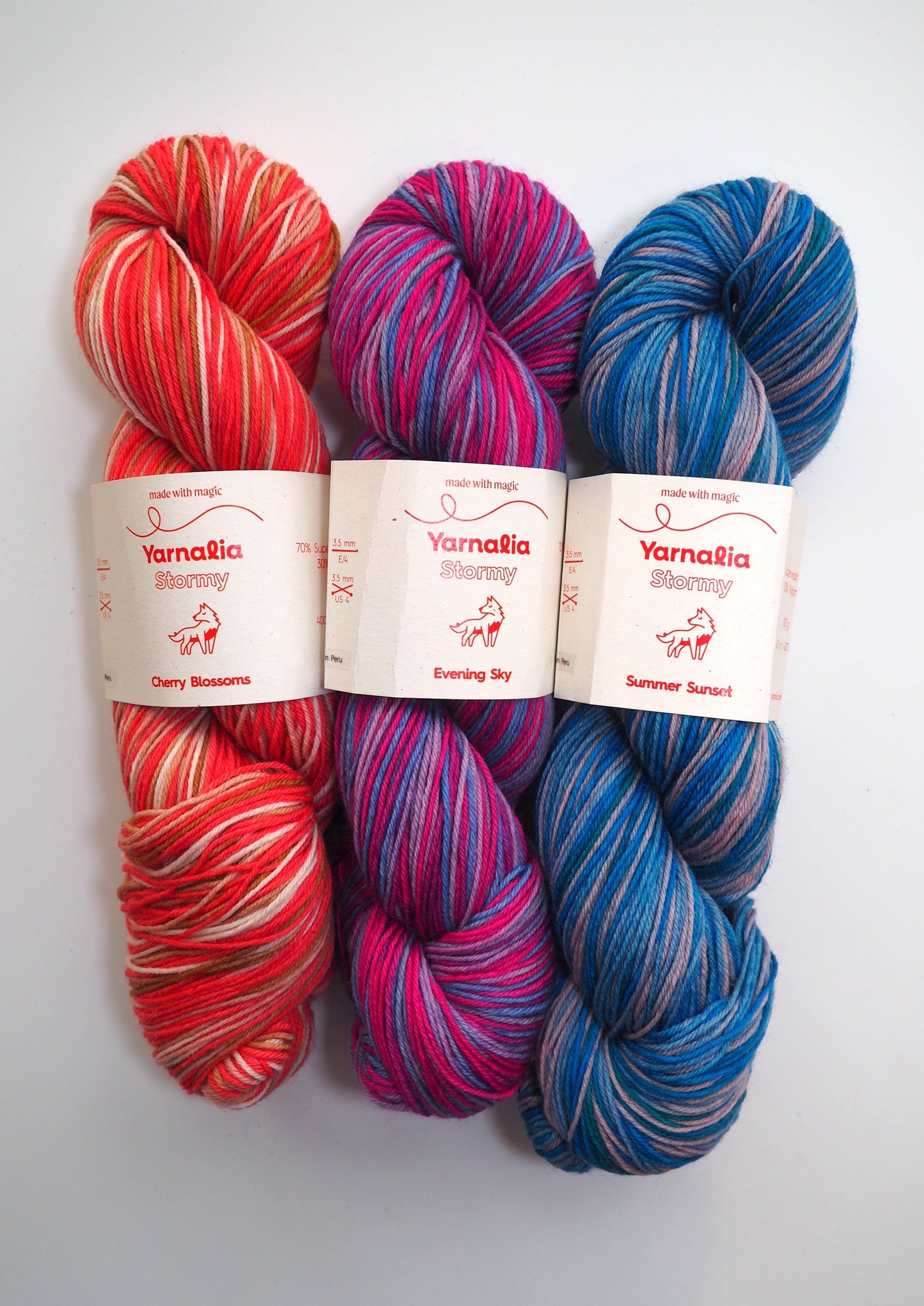 an image of three skeins of Yarnalia Stormy. One red, one pink and blue, and one blue and beige