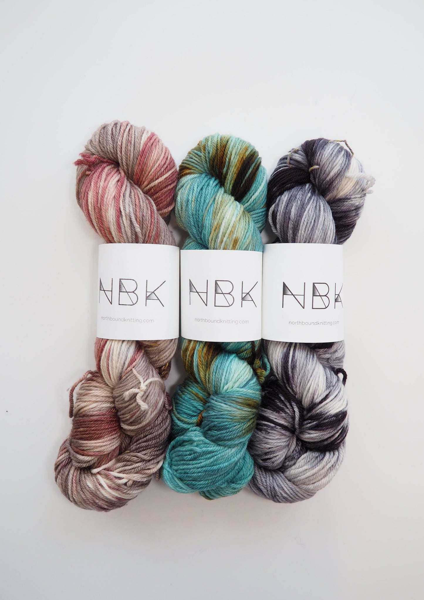 Three skeins of hand-dyed Northbound Knitting Superwash Merino DK yarn in various colors