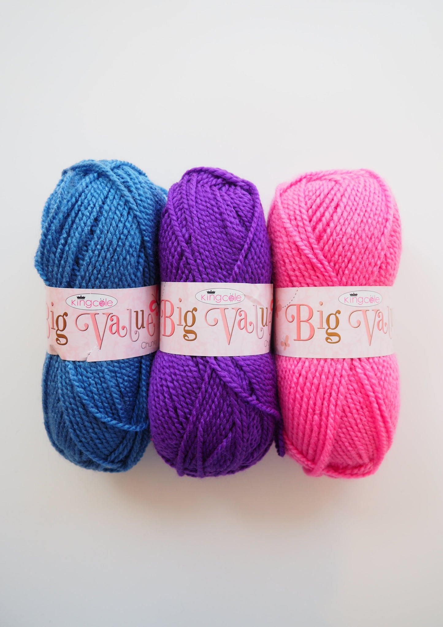 Three balls of King Cole Yarns Big Value Chunky: one in a vibrant blue color, another in a lovely pink shade, and the third in a captivating purple hue.